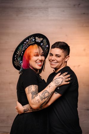 Couple in black attire sharing joyful moment, one wearing decorated wide-brim hat.