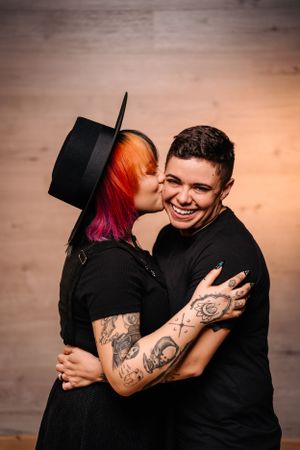 Affectionate couple in black clothing sharing tender moment against wooden backdrop.