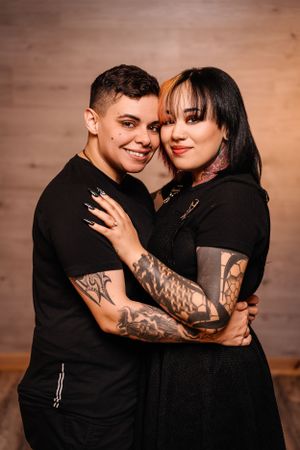 Stylish couple in black outfits embracing and showing affection in studio setting.