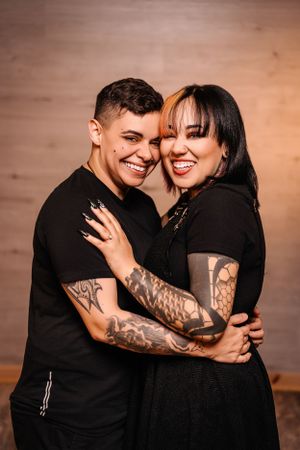 Happy couple in black outfits sharing genuine laughter during intimate photoshoot.