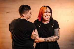 Joyful laughter shared between couple in black outfits against warm-toned background.