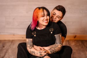 Warm embrace between couple in matching black outfits on wooden floor.