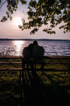 A silhouetted couple watching the sunset over a lake from a bench.