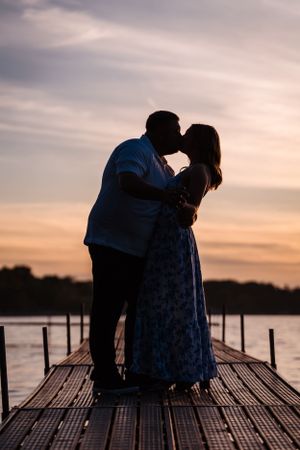 Romantic silhouettes embrace on a wooden dock during sunset over a tranquil lake.