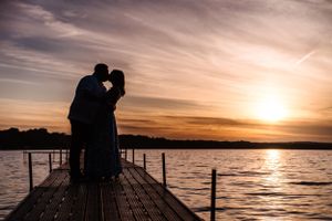 Silhouetted couple shares an intimate moment on pier against dramatic orange sunset sky.