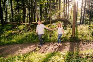 Couple balancing together on fallen log in sunny forest clearing.