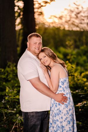 Loving couple poses together at sunset with lush greenery in background.