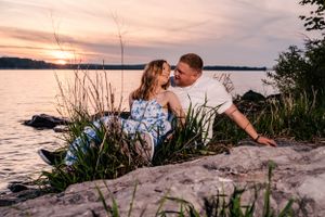 Couple shares intimate moment by lakeside at sunset among tall grass.