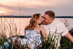 Romantic sunset moment captured by lake with couple among waterside grass.