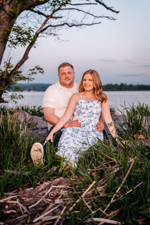 Couple relaxes on lakeside terrain during golden hour with water view.