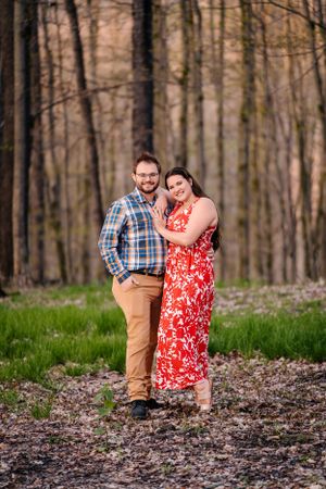 A couple poses together on a wooded path wearing coordinated spring outfits.