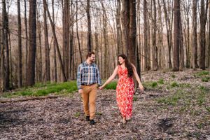 A couple strolls together on a forest path wearing coordinated red dress and plaid shirt.