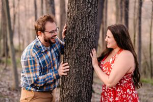 A playful moment between a couple on opposite sides of a tree trunk in coordinated outfits.
