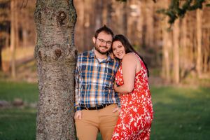 A couple poses against a tree trunk in coordinated outfits during golden hour.