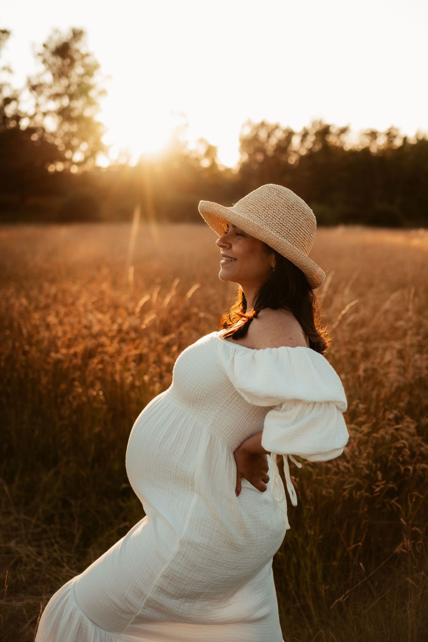 En gravid kvinna på ett fält i solnedgången i en bohemisk klänning och hatt