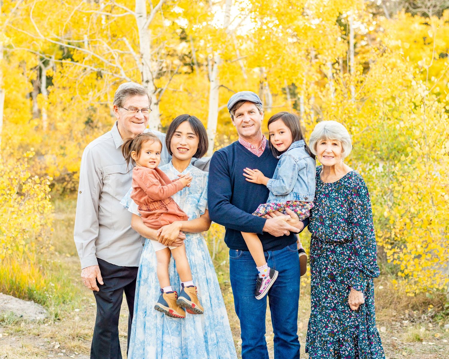 A multi-generational family poses together against a backdrop of yellow fall foliage in alpine loop, Utah.
