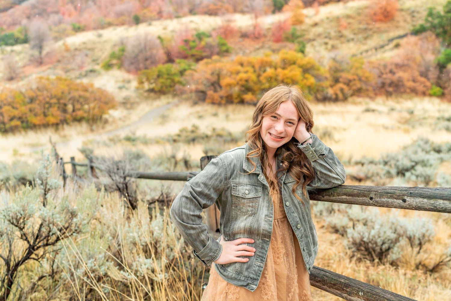 A person poses casually against a rustic fence with autumn mountains in the background at Hidden Valley Park, Utah.