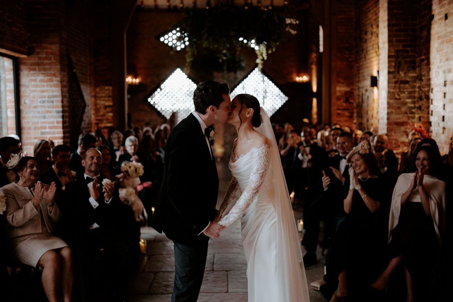A wedding couple stands under a rustic garden arch decorated with flowers and vines.