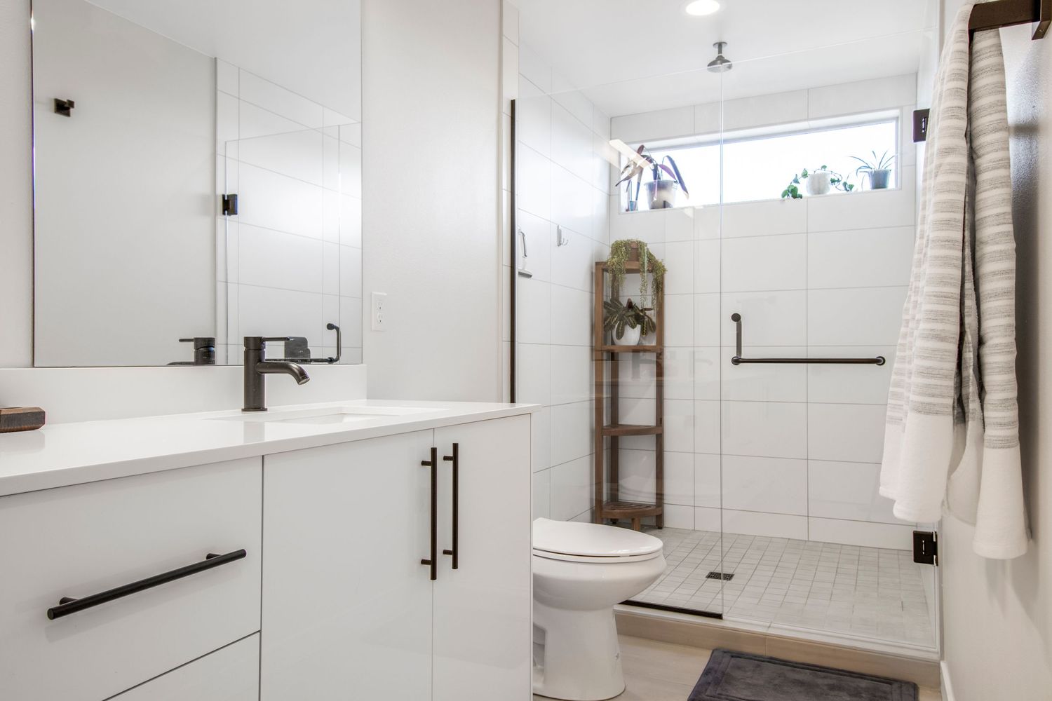 Modern white bathroom with floating vanity, black fixtures, and glass shower enclosure.