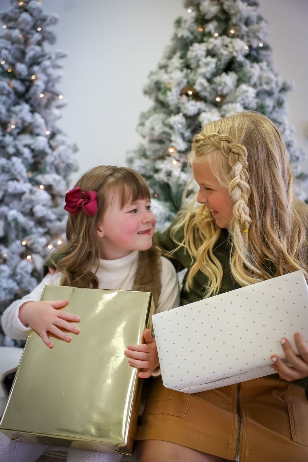 Sweet holiday moment of gift opening in front of snow-flocked Christmas trees.