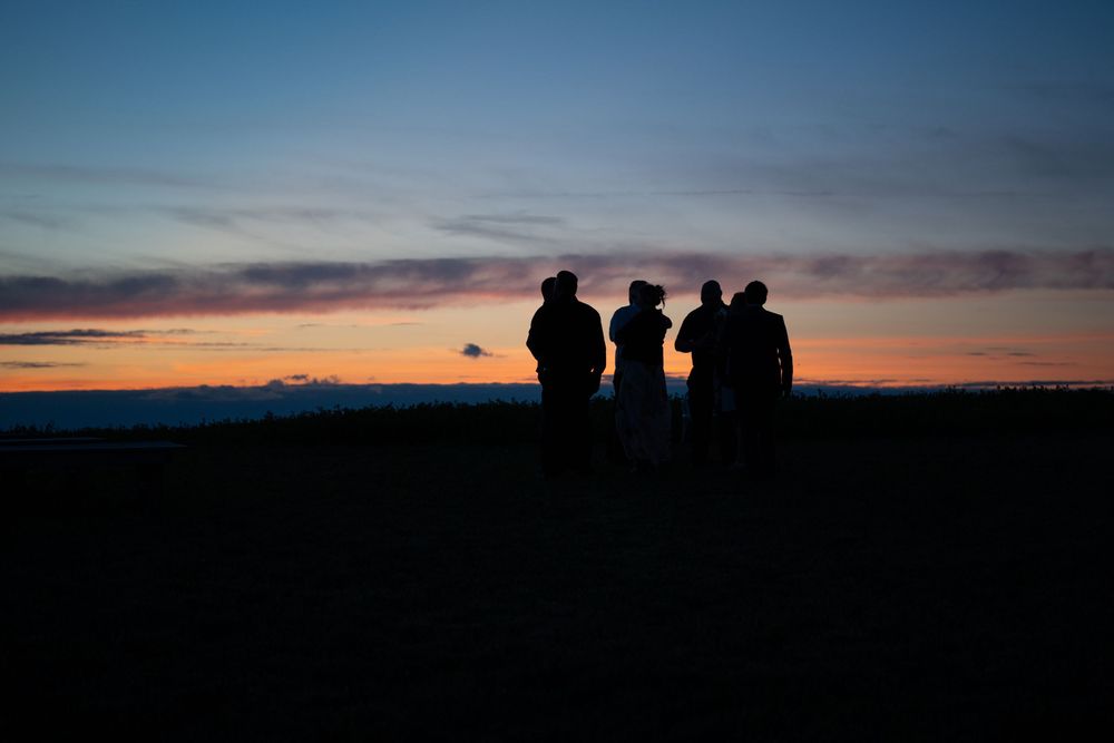 Silhouettes of people standing together against a vibrant sunset sky with dark horizon.