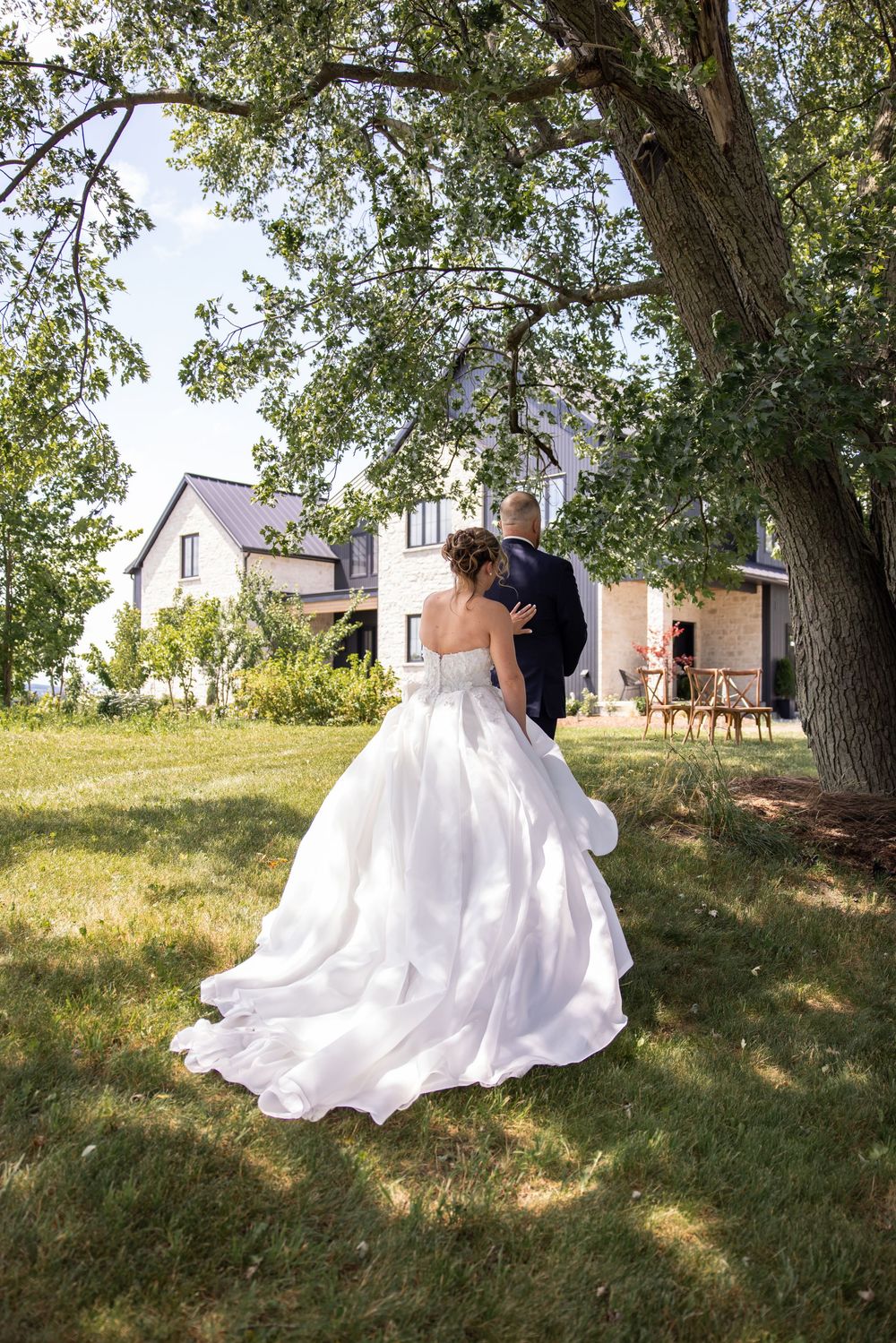 A couple in wedding attire shares an intimate moment under trees on a grassy hillside.