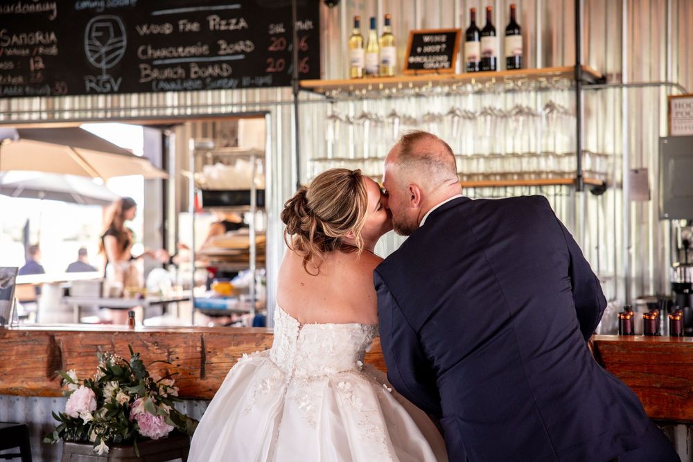A couple shares a romantic moment during their wedding reception at a rustic venue with wine bottles in the background.