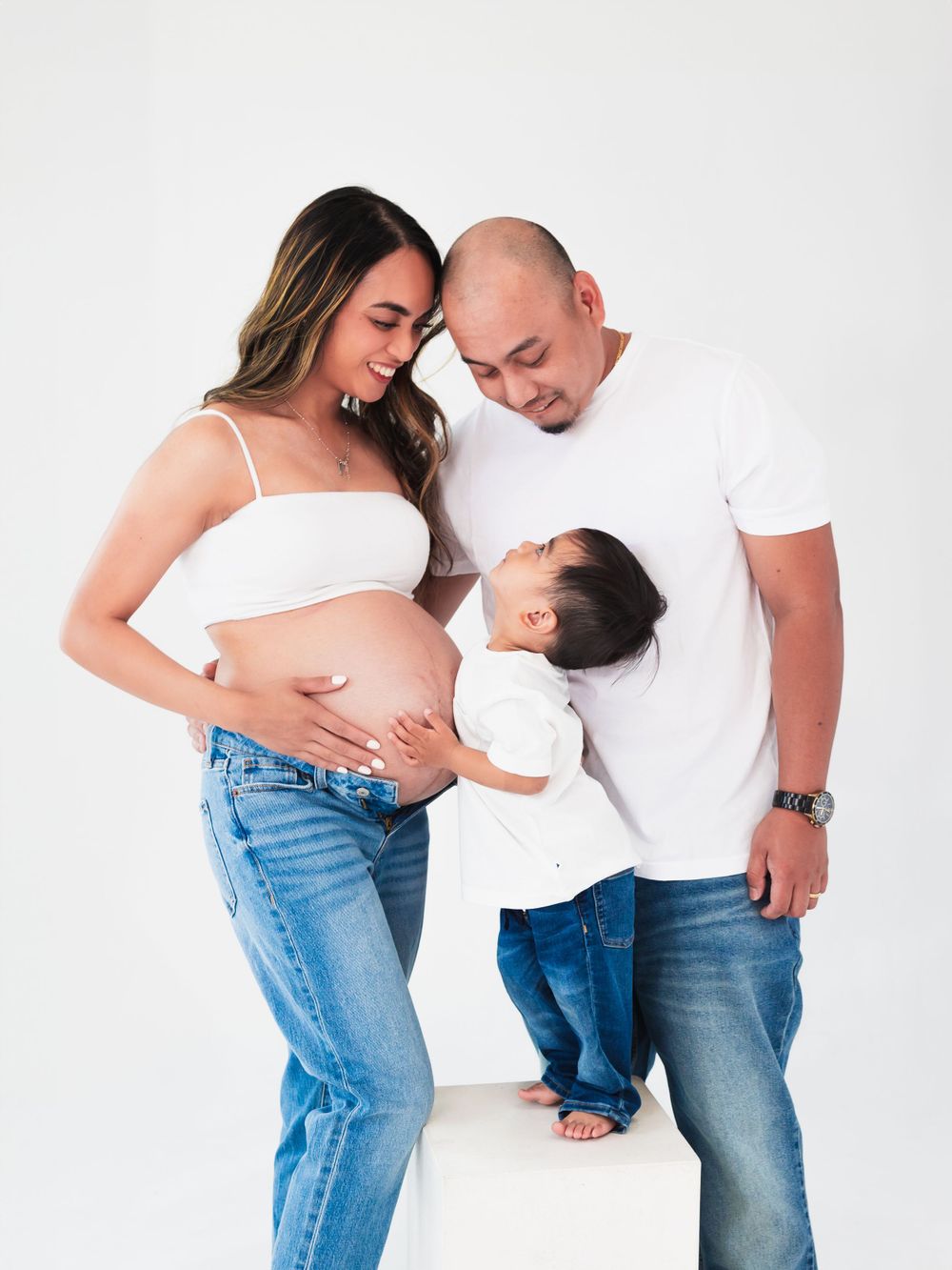 Expecting parents with their young child sharing a loving moment in a minimalist maternity photoshoot. Toronto maternity photography.