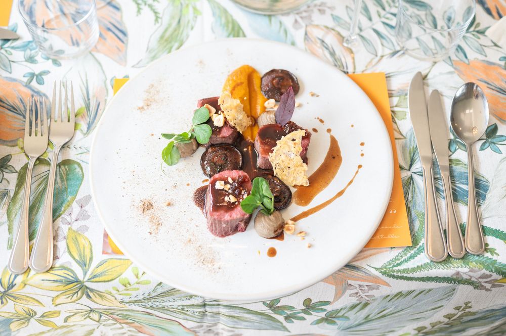 Elegant plated dessert with chocolate rolls, caramel sauce, and mint garnish served on white china with floral tablecloth.