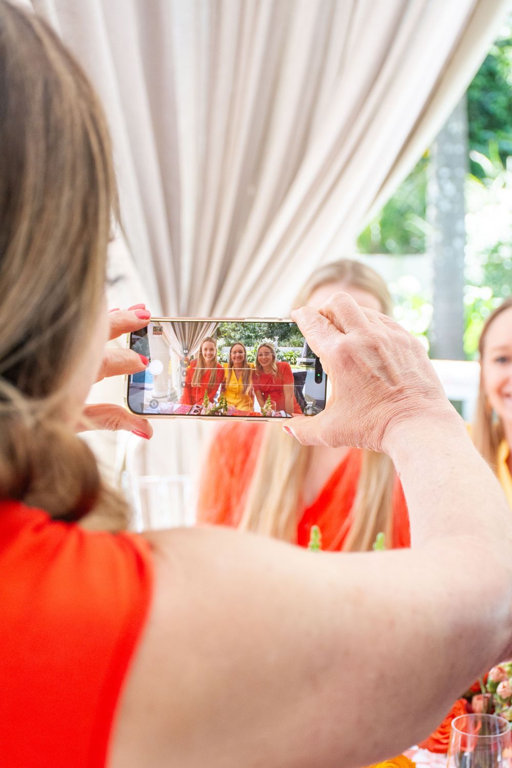 Person taking photos with smartphone at an outdoor social gathering with white tent decor.
