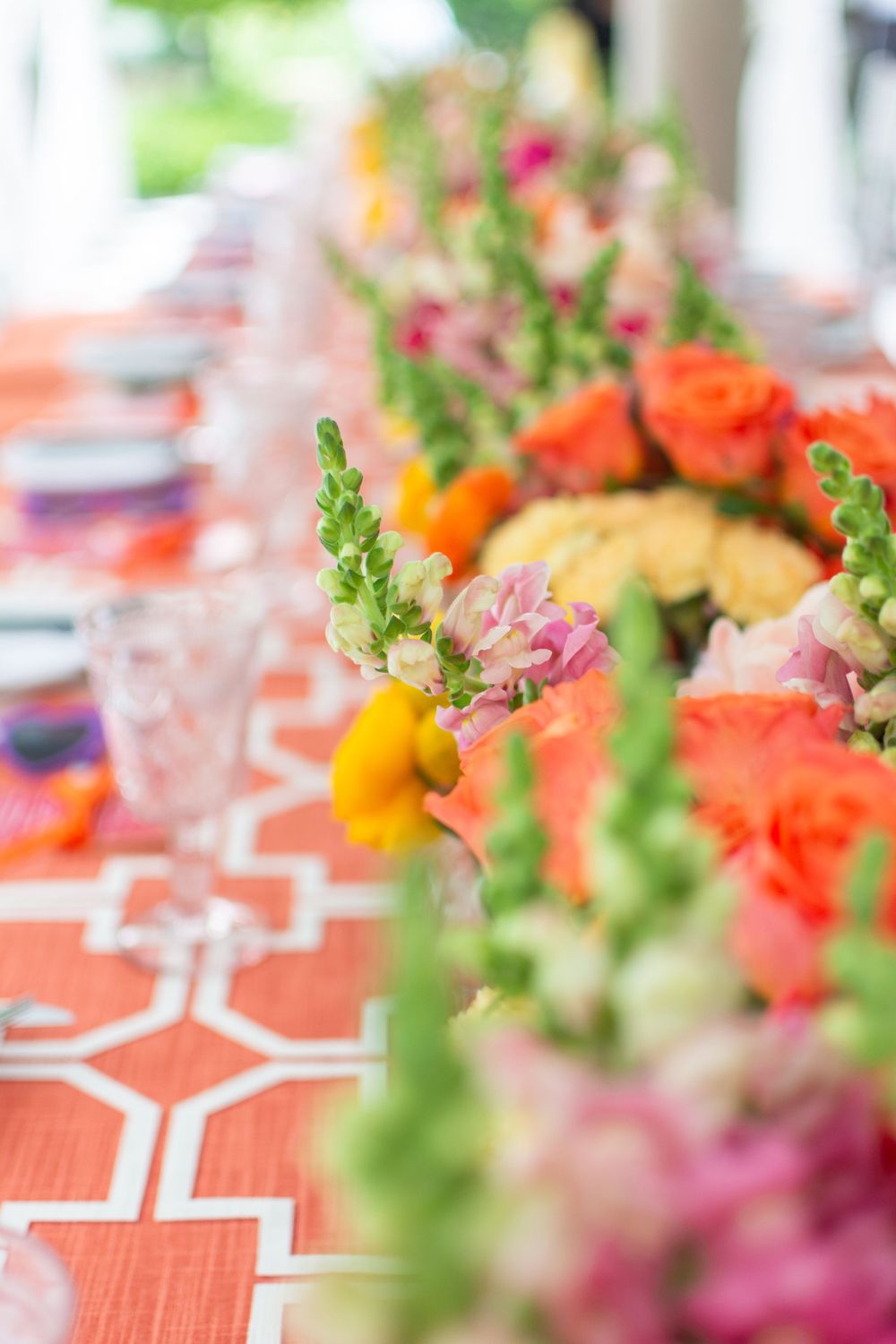 Colorful floral centerpieces with orange and pink blooms arranged on coral patterned tablecloths at an elegant event.