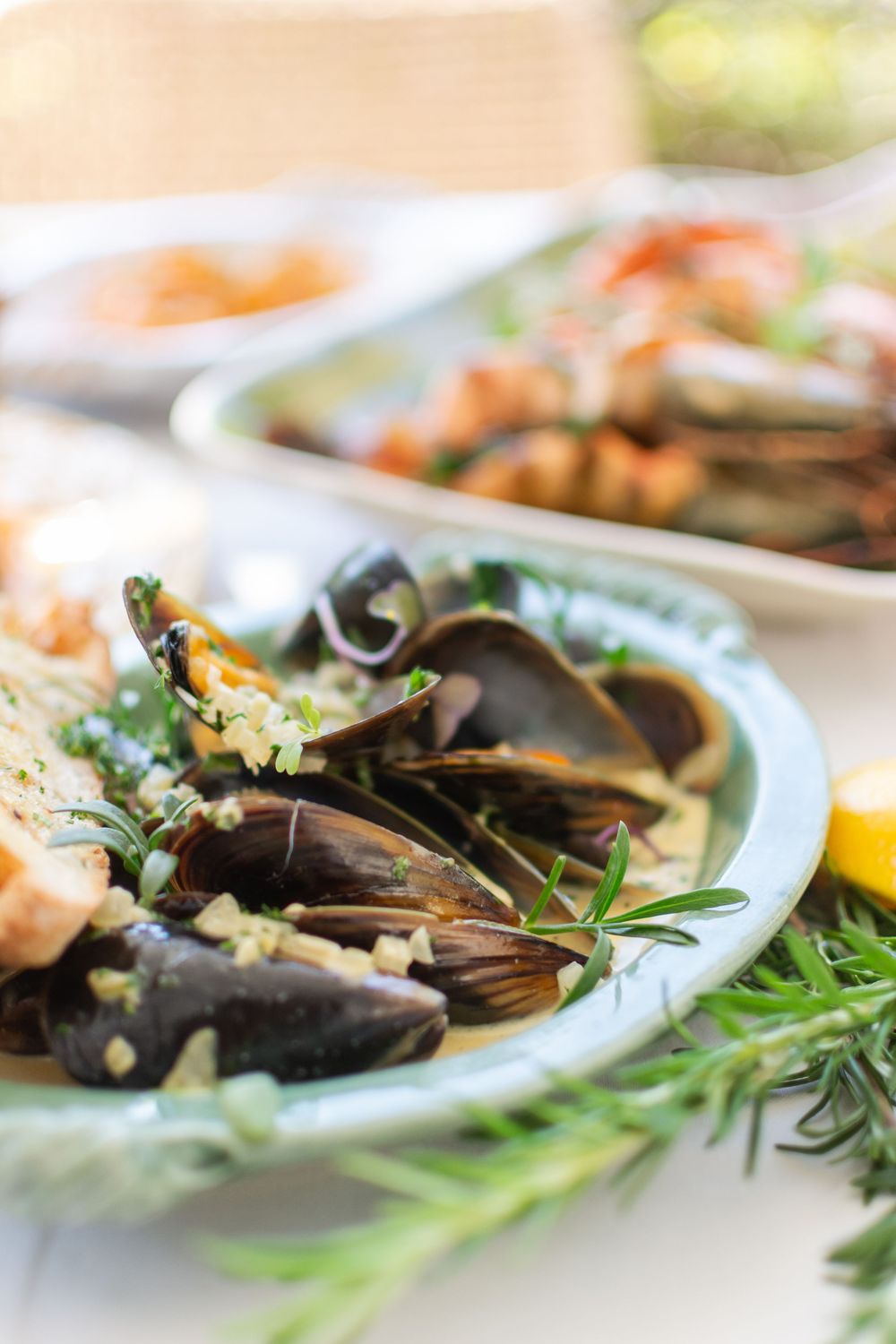 Close-up view of steamed mussels garnished with fresh herbs and lemon on a white plate.