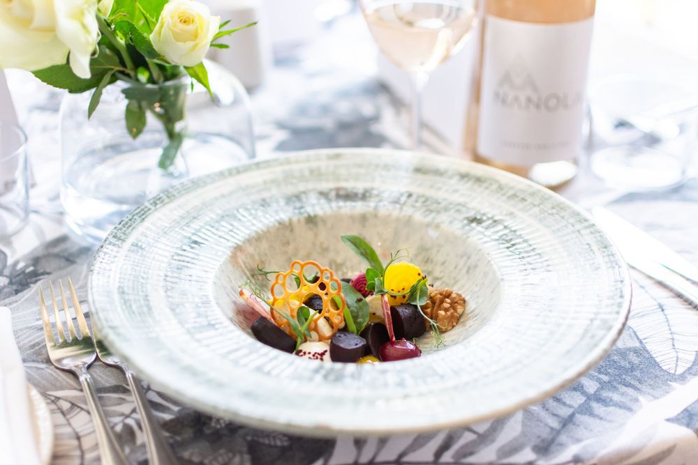 An elegant plated fine dining dish with colorful garnishes on a white decorative plate next to floral decor.