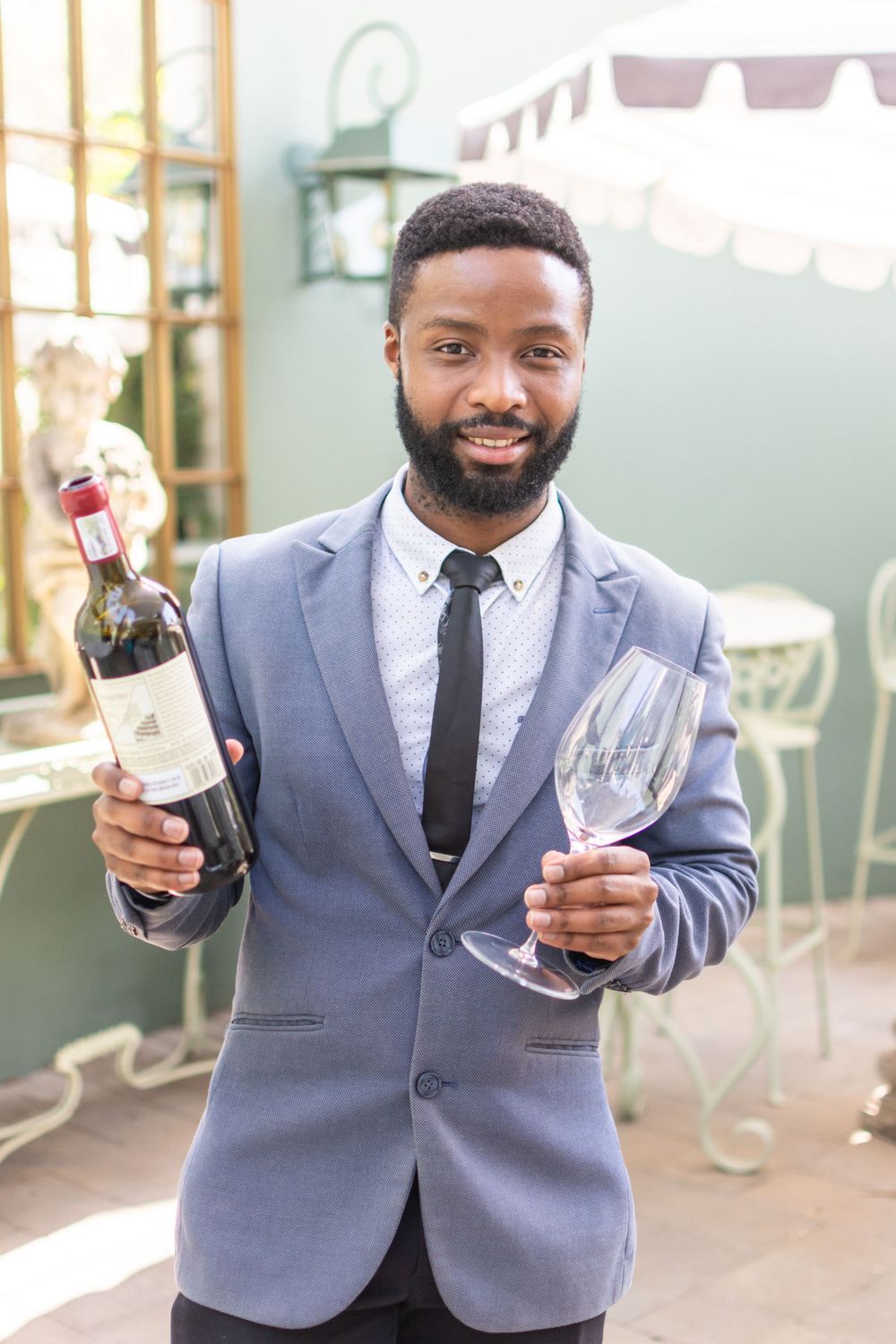 Professional in a gray suit holding a wine bottle and glass in an elegant indoor setting.