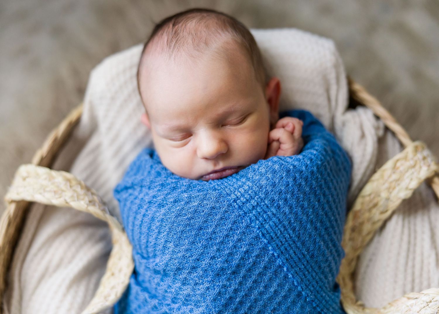Sleeping newborn baby wrapped in blue blanket nestled in cozy basket.