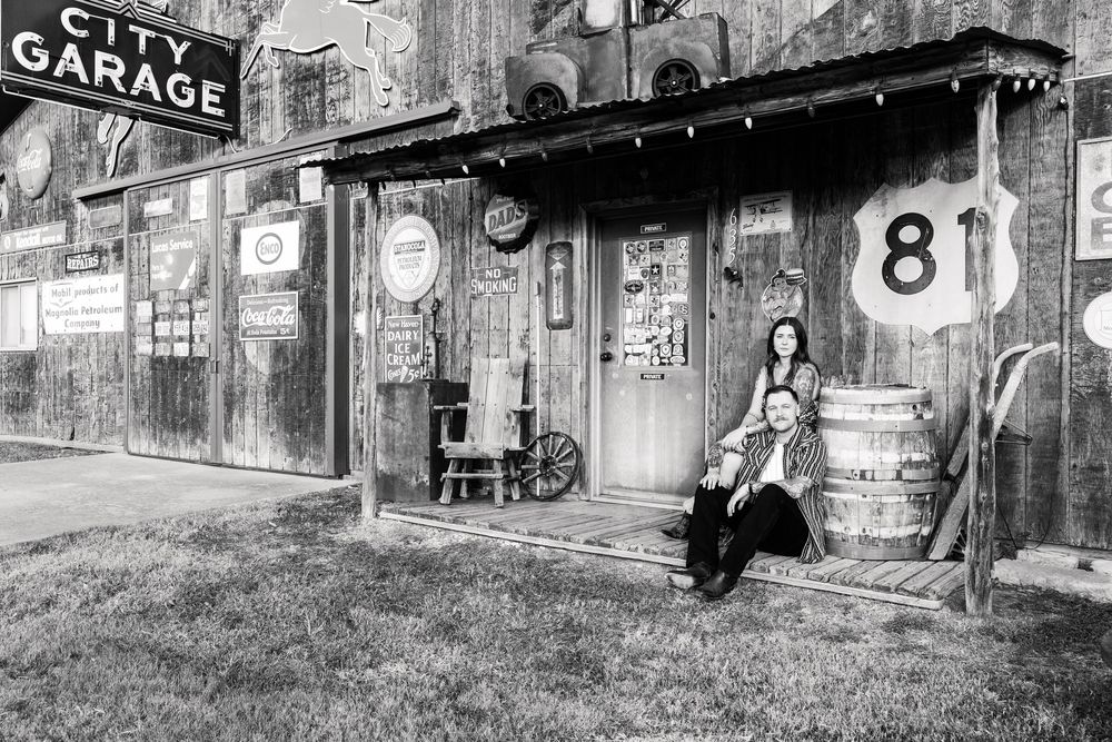 A vintage black and white photograph of a rustic garage storefront with Route 81 sign and someone sitting outside.