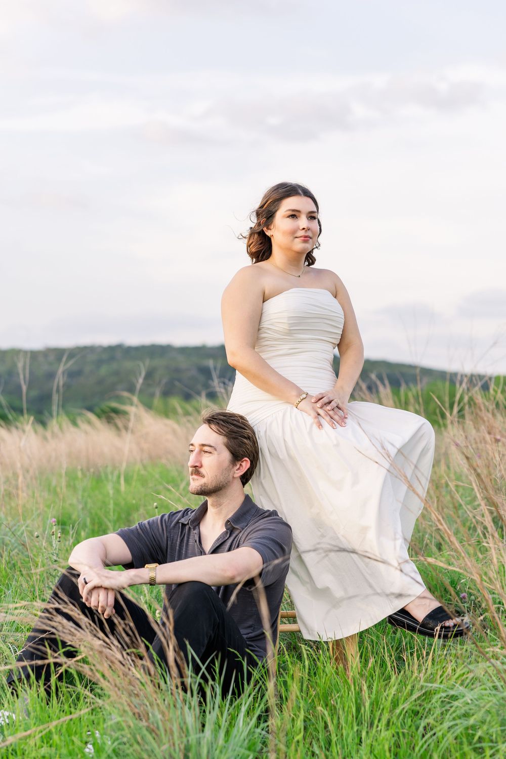 A couple relaxes together in a scenic grassy meadow on a cloudy day.