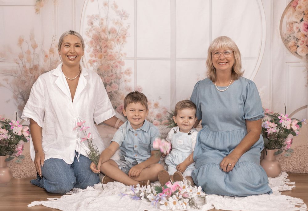 Family portrait with floral decorations featuring adults and children sitting together on floor with pink roses and decor.