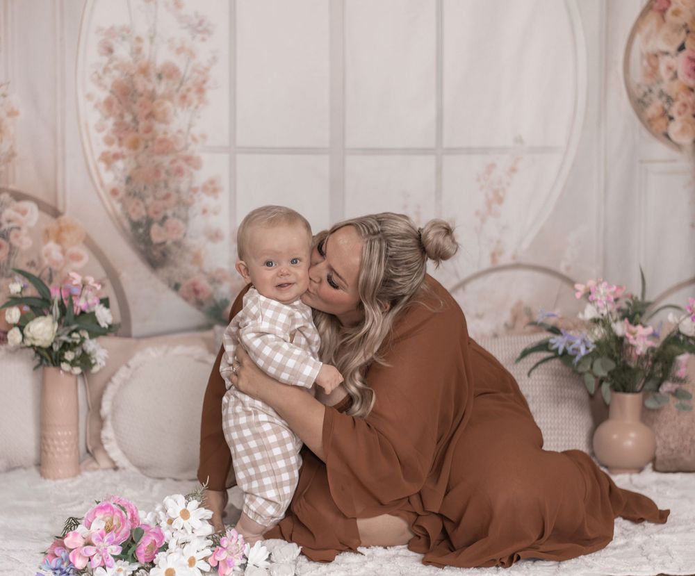 Tender maternal moment in a floral decorated room with brown blanket and pink flowers in soft lighting.