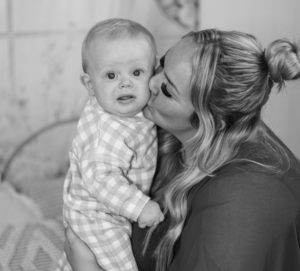 A tender black and white moment shared between parent and baby in plaid outfit, captured in intimate indoor portrait.