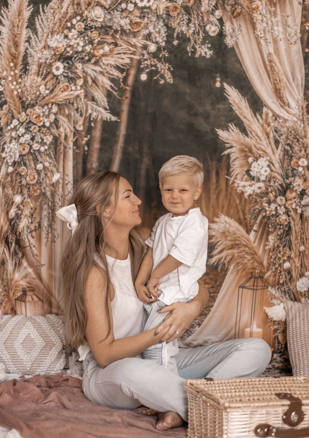 A mother and young boy pose together in a boho-styled floral backdrop with pampas grass and warm tones.