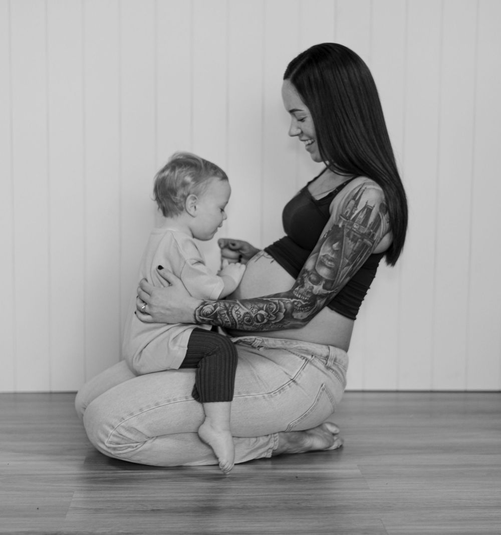 A black and white portrait of a parent and small child sharing a tender moment on a hardwood floor.