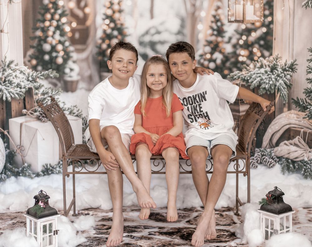 Children sitting together on a rustic wooden bench in a cozy winter holiday setting with snowy decorations.