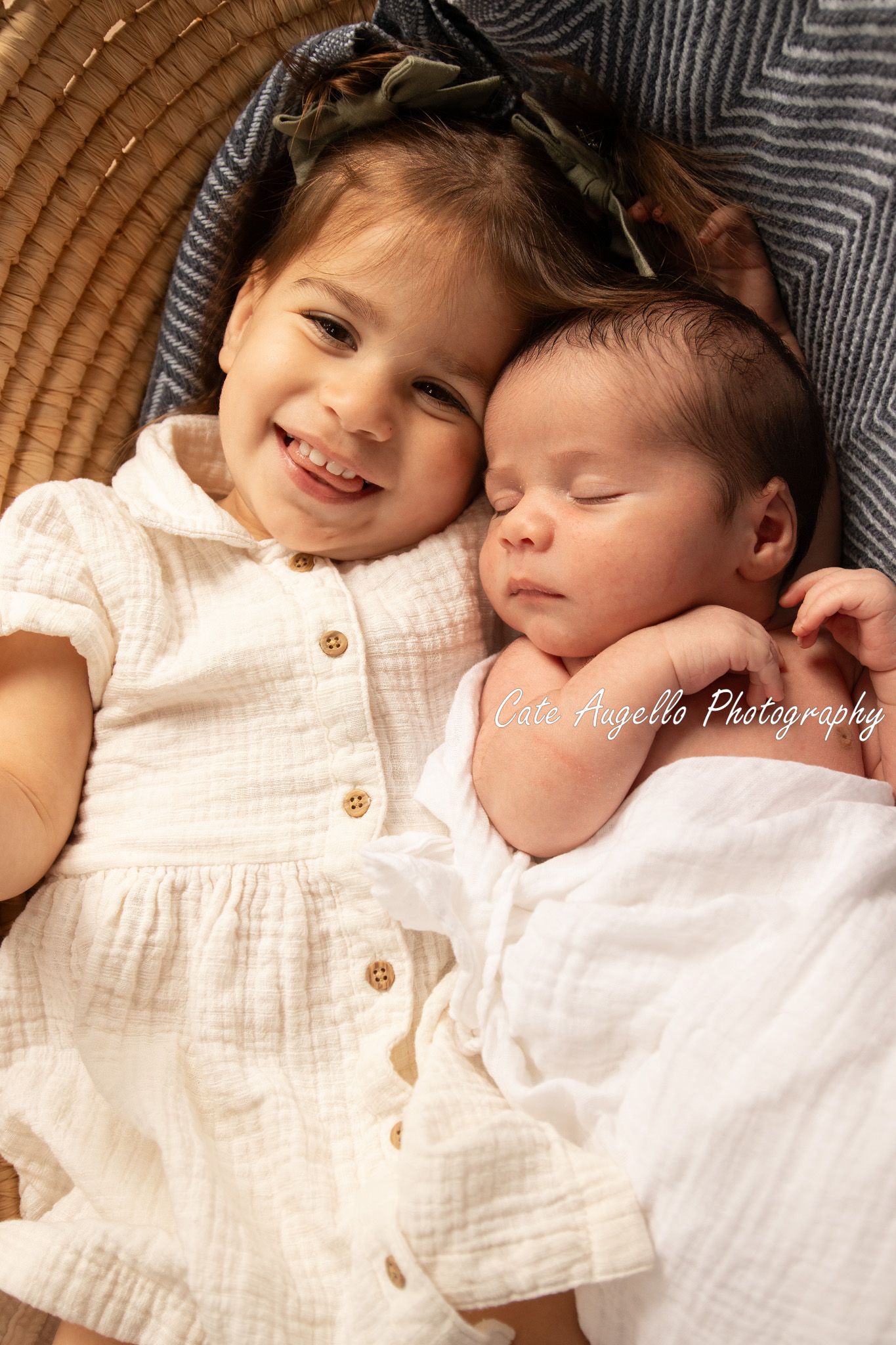 Two siblings in white clothing laying together on a textured brown surface, one awake and one sleeping peacefully. Newborn photo Enfield, CT