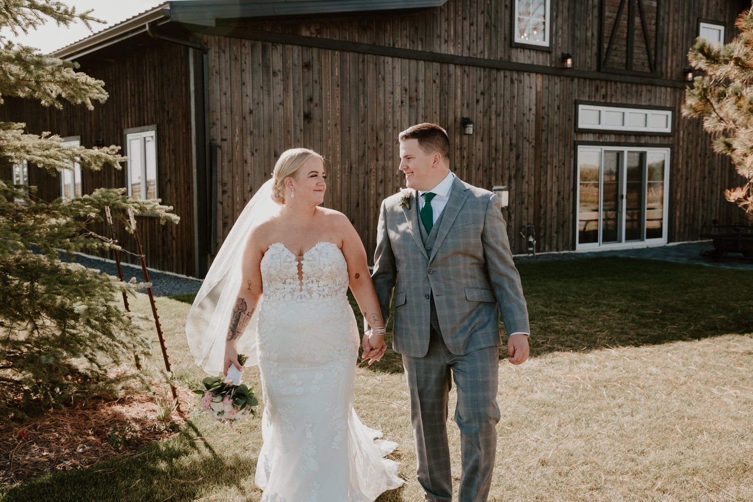 Bride and groom walking hand in hand looking at each other.