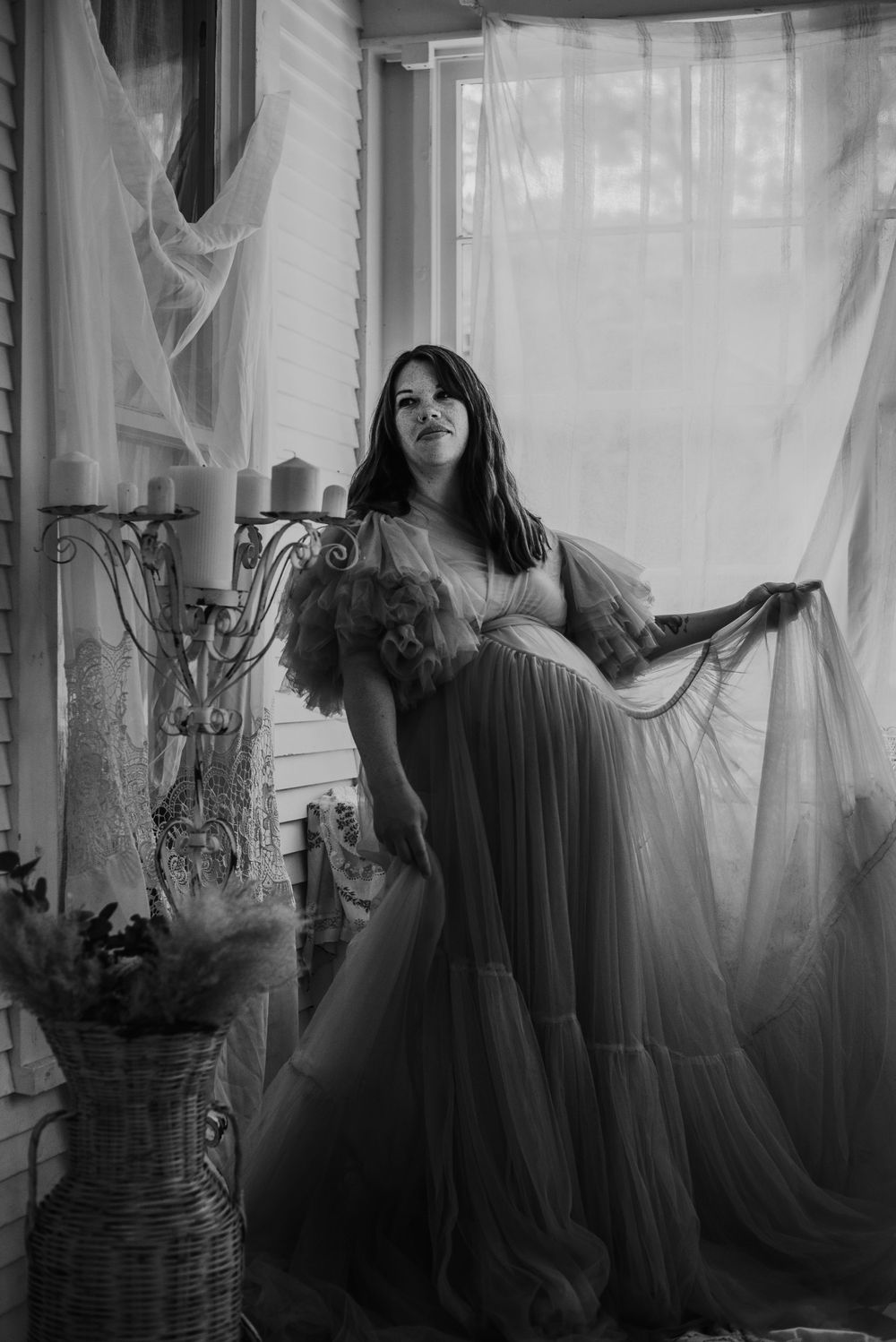 Expecting mother holds her bump and sways with her flowy dress as the sun highlights her bump from behind