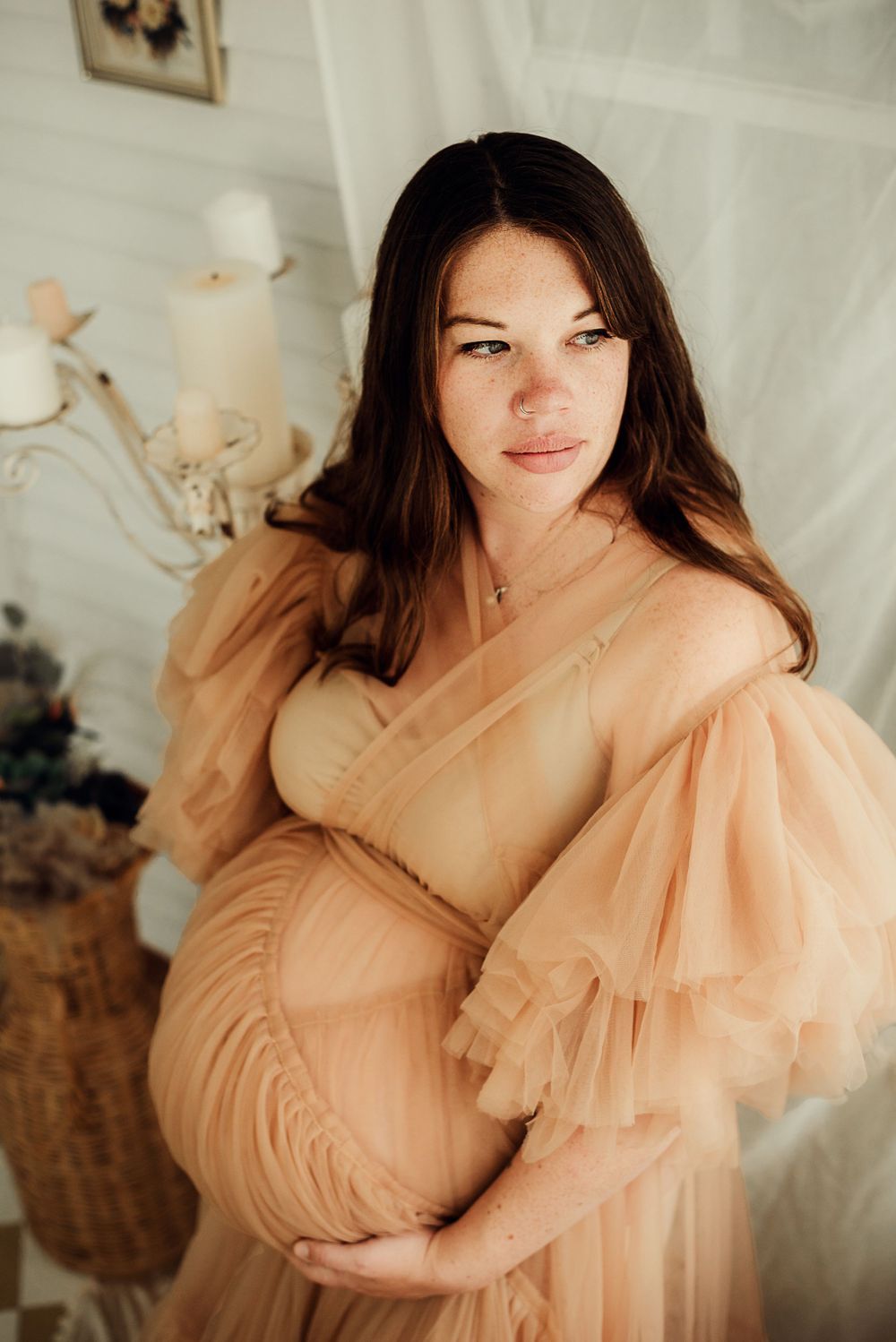 New mother in impactful dress holds her baby bump and looks out the window during maternity session