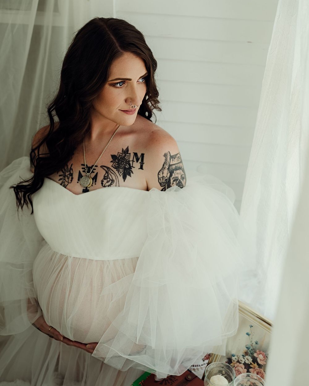 New mother in impactful dress holds her baby bump and looks out the window during maternity session