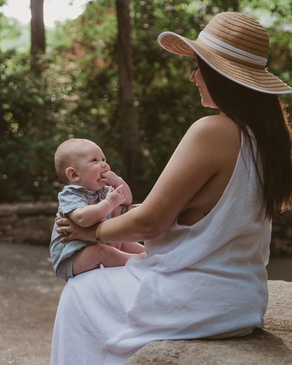New mom sits on a bench and plays with smiling baby during a nursing session