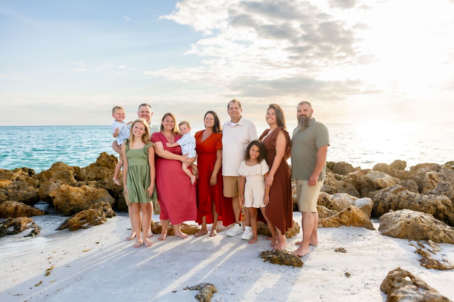 Happy family of seven posing together on a white sand beach at sunset.